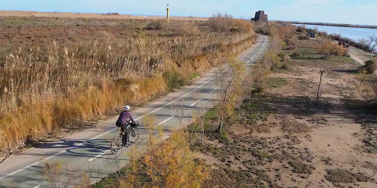 Vista aérea de ciclista en carril bici asfaltado hacia la desembocadura del río Ebro y el mirador del Zigurat