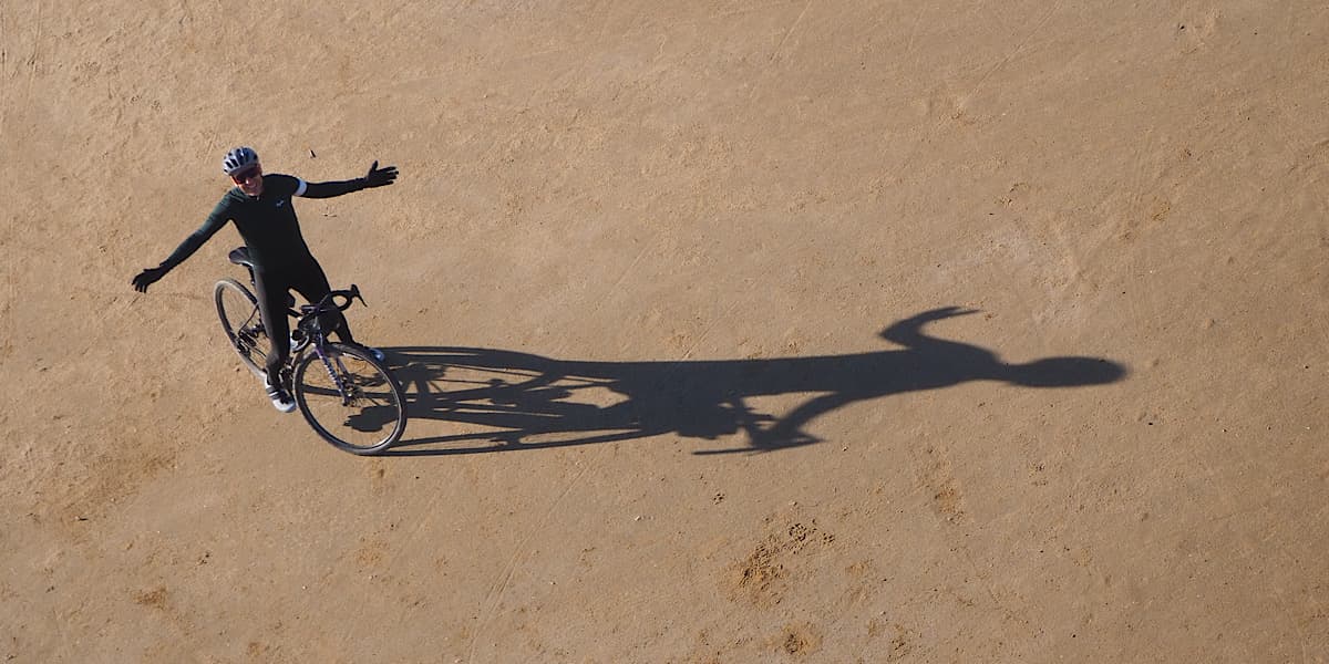 Vista cenital de ciclista abriendo los brazos sobre la arena con una larga sombra proyectada en la playa del Delta del Ebro
