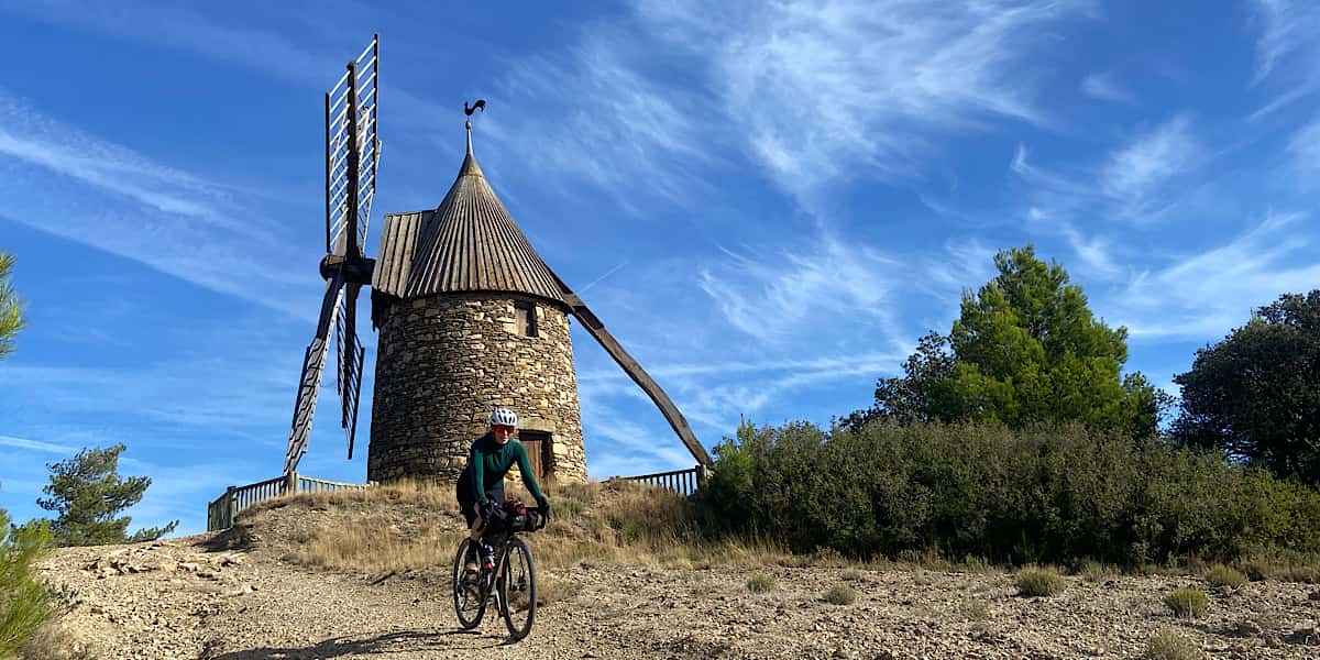 Cicloturista pedaleando junto a un antiguo molino de piedra camino a Labastide en la ruta PassaPaïs y La Véloccitanie